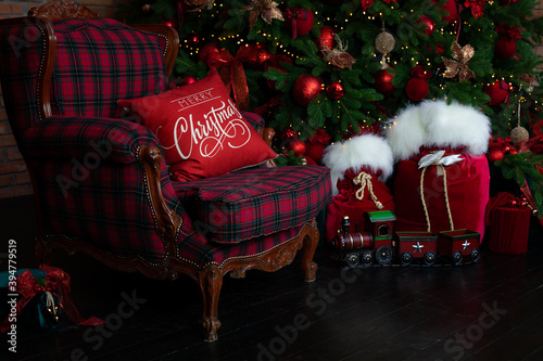 Stylish loft interior of room with Christmas fir tree and checkered armchair. Red sack santa claus with gifts near big Christmas fir. Beautiful decorated living room for Christmas. holiday celebration photo