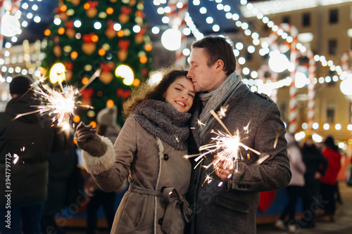 Couple in love having fun with sparklers on christmas decoration lights street. Romantic date for Valentine's day Outdoors. Young man and Woman laughing. Winter wonderland city  scene. New Year party