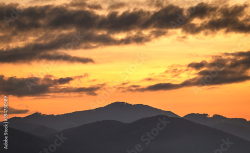 Colorful sky with clouds over the silhouettes of the hills at sunset.