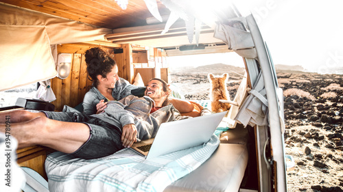 Hipster couple with dog traveling together on retro mini van transport - Digital nomad concept with indie people on minivan romantic trip working at laptop pc in relax moment - Warm contrast filter