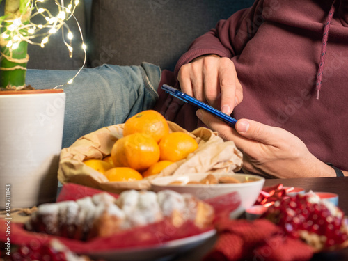 Closeup view of man with mobile phone sitting near Christmas decorated table 