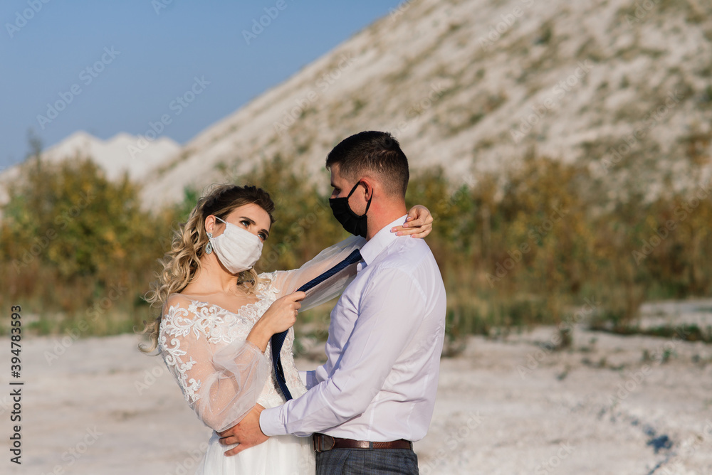 Young loving couple in medical masks in park during quarantine on wedding day. Young loving couple in medical masks in park during quarantine on wedding day.