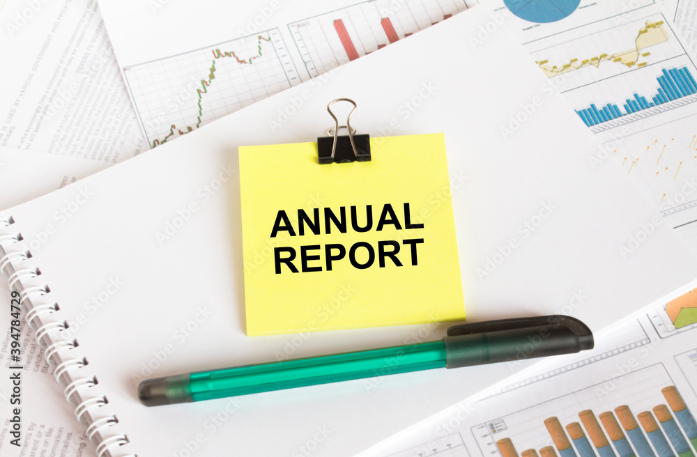 A yellow sticker with text Annual Report is in a Notepad with a green pen financial charts and documents A yellow sticker with text Annual Report is in a Notepad with a green pen financial charts and documents