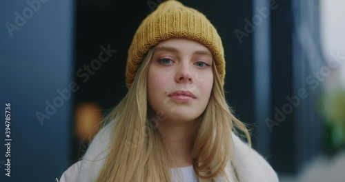 Serious young attractive smile woman with hat look at camera at city center feel happy. Fshion girl. Stand on street. Cute face. CLose up. Slow motion photo