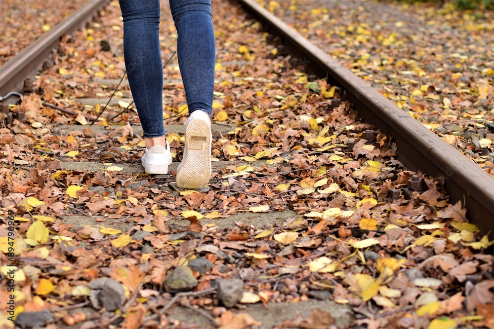 Fototapeta premium Walking legs wearing blue jeans and white shoes on autumn leaves