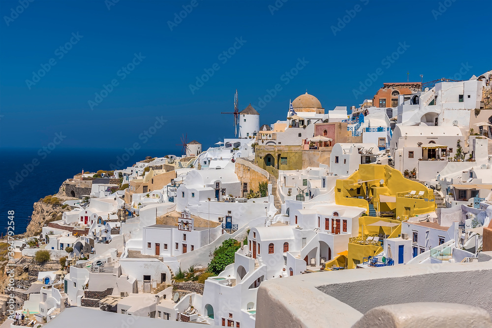 Windmils, dome churches and dazzling white buildings in the village of Oia, Santorini in summertime