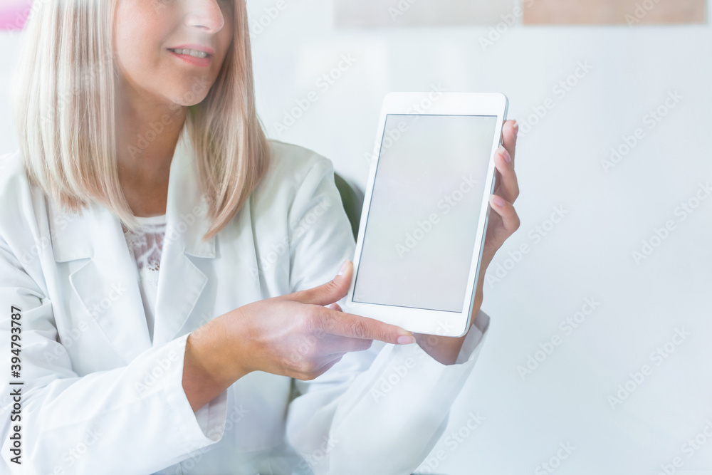 Pretty blonde nurse in medical uniform with tablet, copy space on empty white wall