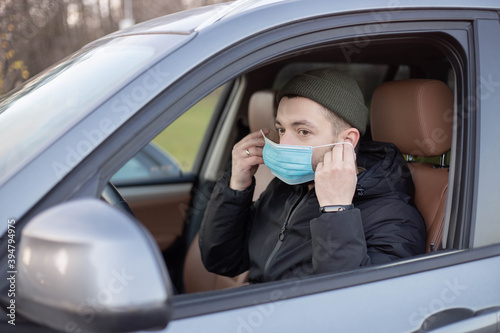 Male driver wearing mask in car during coronavirus outbreak.White bearded man wearing protective mask to avoid the infection of virus and polluted air spreading deseases inside of his car.  © Julija