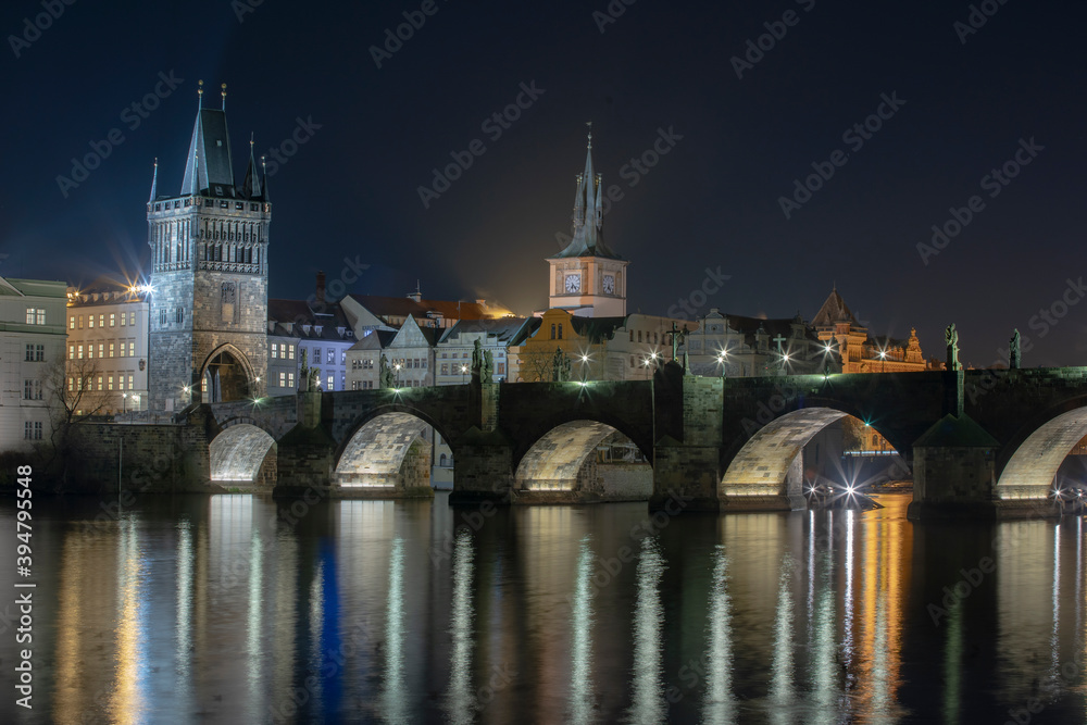 
illuminated Charles Bridge from 14 centuries and light from street lighting and stone sculptures on the bridge and light reflections on the surface of the Vltava river at night in Prague
