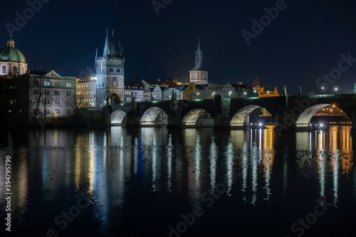  illuminated Charles Bridge from 14 centuries and light from street lighting and stone sculptures on the bridge and light reflections on the surface of the Vltava river at night in Prague