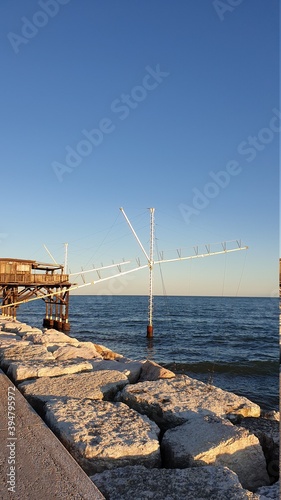Traditional fishing station house with fishnet in water of Adriatic sea at pier Diga Sottomarina, skyline with beach, amazing yellow red sunset at twilight, dusk, evening view, Northern Italy