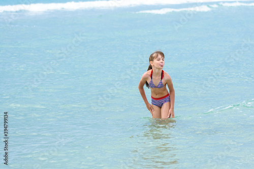 A girl stands knee-deep in sea water  does not want to go out to bask and sticks out her tongue