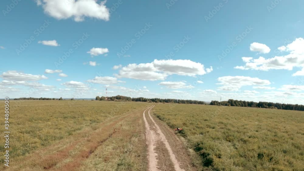 Camera chase follows fpv racing drone doing tricks at fly above green field with rural road under blue sky with clouds first point view. Camera chase follows fpv racing drone doing tricks at fly above green field with rural road under blue sky with clouds first point view.