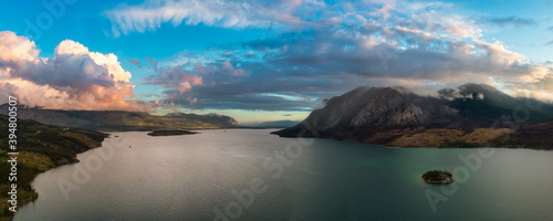 Beautiful Panoramic View of Lake alongside Scenic Road surrounded by Mountains and Trees. Dramatic Sunrise Sky. Aerial Drone Shot. Taken near Klondike Highway, Southern Yukon, Canada.