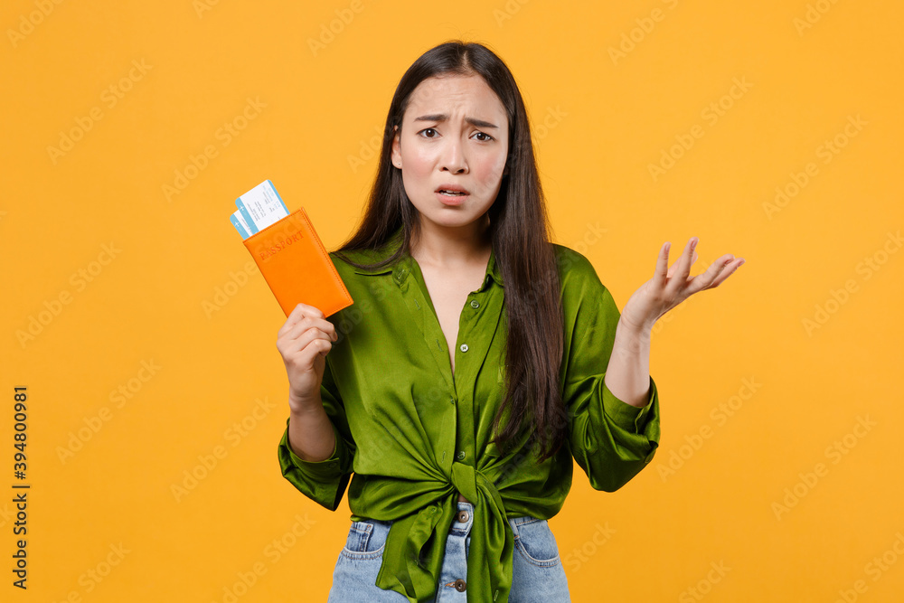 Displeased young traveler tourist asian woman in green shirt hold passport tickets spreading hands isolated on yellow background. Passenger traveling on weekends getaway. Air flight journey concept. Displeased young traveler tourist asian woman in green shirt hold passport tickets spreading hands isolated on yellow background. Passenger traveling on weekends getaway. Air flight journey concept.