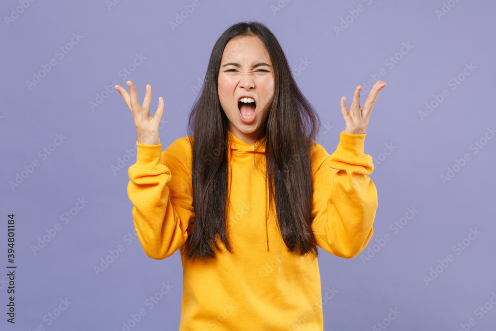 Angry irritated young brunette asian woman wearing casual basic yellow hoodie standing spreading hands screaming swearing looking camera isolated on pastel violet colour background studio portrait. Angry irritated young brunette asian woman wearing casual basic yellow hoodie standing spreading hands screaming swearing looking camera isolated on pastel violet colour background studio portrait.