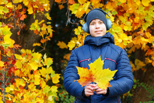 portrait of a teenager listening to music by headphones  relaxing in autumn city park  bright yellow maple leaves as background