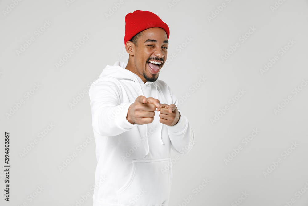 Cheerful blinking young african american man 20s years old wearing casual basic streetwear hoodie standing pointing index fingers on camera isolated on white colour wall background studio portrait. Cheerful blinking young african american man 20s years old wearing casual basic streetwear hoodie standing pointing index fingers on camera isolated on white colour wall background studio portrait.