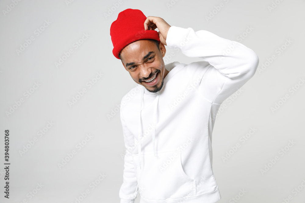 Smiling cheerful young african american man 20s years old wearing basic casual streetwear hoodie standing put hand on head looking camera isolated on white colour wall background, studio portrait.