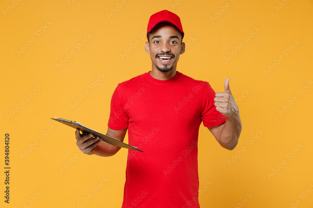 Delivery employee african man 20s in red cap blank print t-shirt uniform workwear work courier dealer service concept hold in hand clipboard with papers document isolated on yellow background studio.