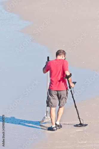 back view, far distance of a male walking a tropical, sandy beach shoreline with a metal detector, searching for metal objects and coins, on gulf of Mexico, on a sunny afternoon