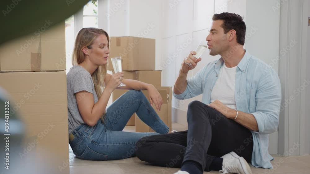 Couple taking a break on moving day sitting on floor surrounded by boxes and making a toast with champagne - shot in slow motion Couple taking a break on moving day sitting on floor surrounded by boxes and making a toast with champagne - shot in slow motion