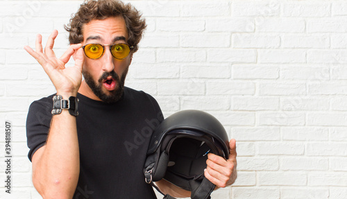 young man feeling shocked, amazed and surprised, holding glasses with astonished, disbelieving look photo