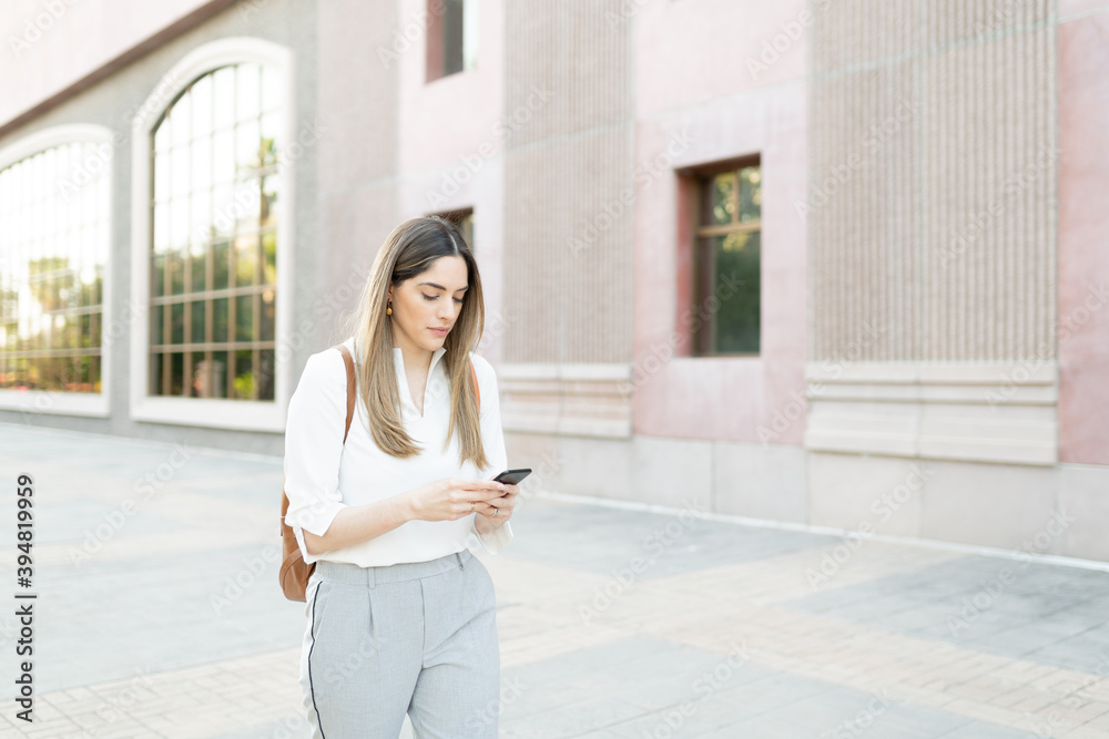 Pretty female worker in her 30s walking while sending a text Pretty female worker in her 30s walking while sending a text