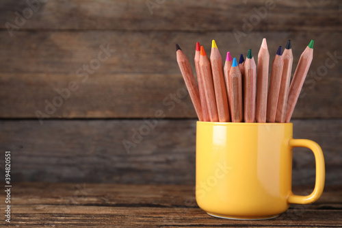 Colorful pencils in cup on wooden table. Space for text