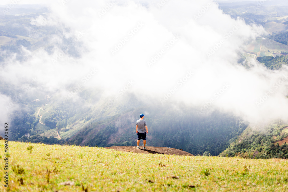 Man on the top of a mountain, looking at the valley with lots of clouds Man on the top of a mountain, looking at the valley with lots of clouds