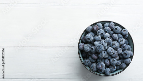 Canvas Print Tasty frozen blueberries in bowl on white wooden table, top view
