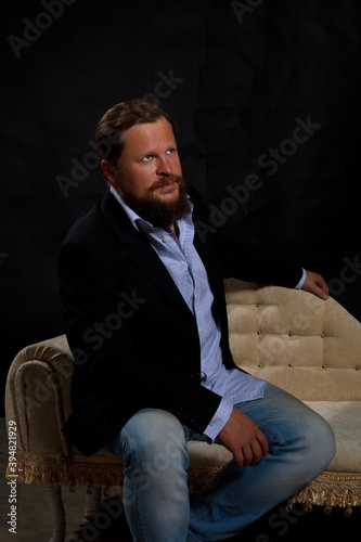 Thoughtful solid bearded man dressed in suit sitting on sofa