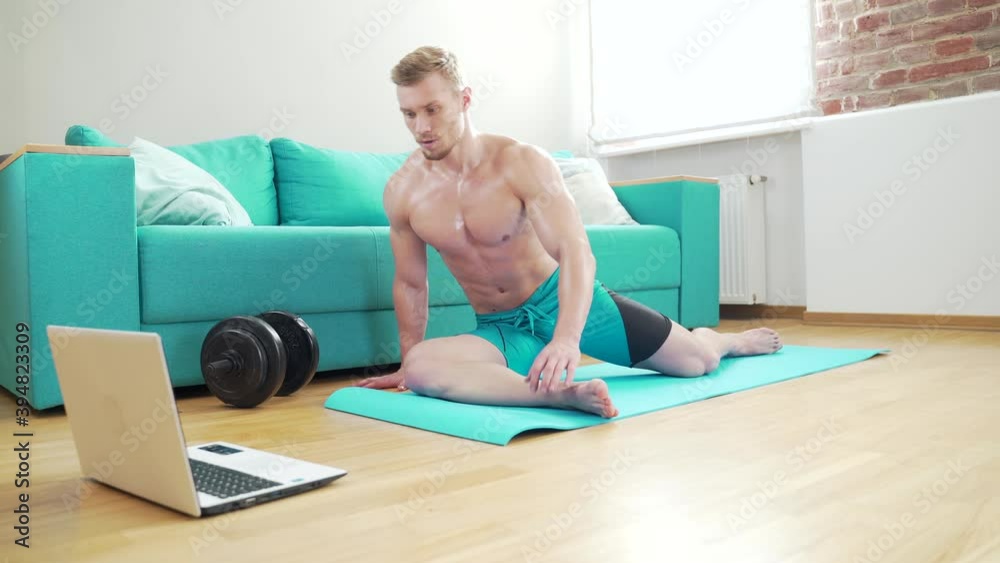 Young fitness male athlete practicing online yoga exercises on floor a ...
