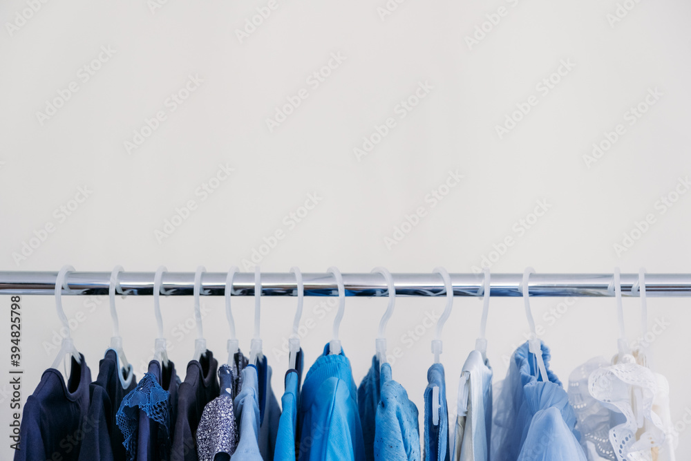 Fast fashion, Sustainable fashion, minimalist wardrobe. Variety of female blue clothing on hanging on white background with copy space. Fashion minimal style banner Fast fashion, Sustainable fashion, minimalist wardrobe. Variety of female blue clothing on hanging on white background with copy space. Fashion minimal style banner