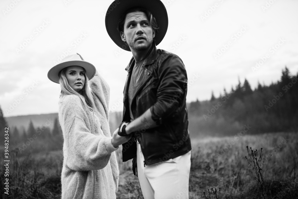 © shunevich - Handsome man and beautiful woman walking at the field, wearing hats, enjoy weekend together, loving husband gently hold a hand of adorable wife, fashionable couple concept