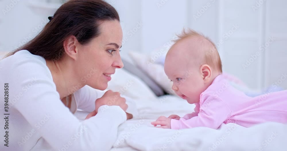 Portrait, a young beautiful mother is talking with her newborn baby and smiling at her. Newborn baby lies on a light bed and looks at her mother, happy motherhood. 4k, ProRes Portrait, a young beautiful mother is talking with her newborn baby and smiling at her. Newborn baby lies on a light bed and looks at her mother, happy motherhood. 4k, ProRes