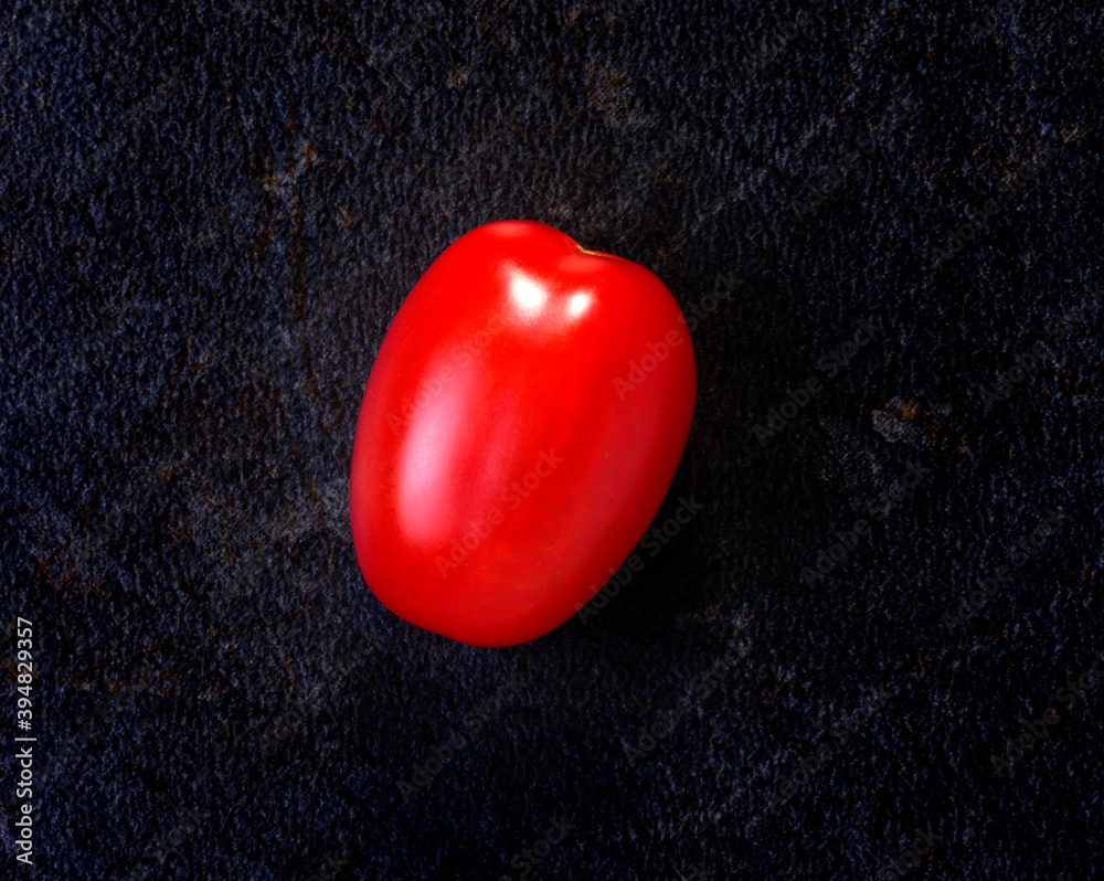 A single small red tomato on a dark ceramic tile A single small red tomato on a dark ceramic tile