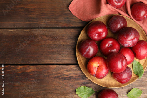 Delicious ripe plums on wooden table, flat lay. Space for text