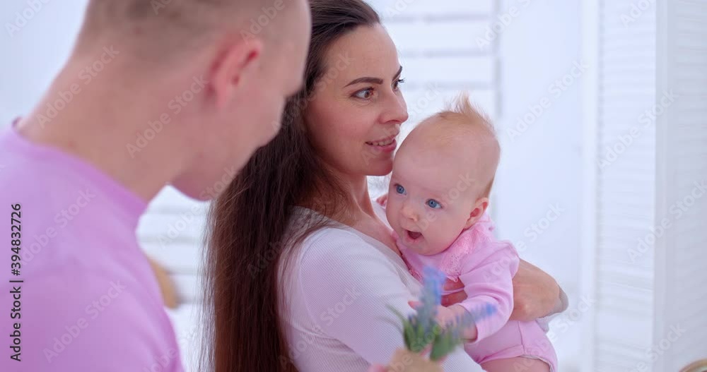 Portrait, a beautiful mother stands with a little daughter in her arms. Dad gives flowers to his little daughter, the baby smiles. Family values. 4k, ProRes Portrait, a beautiful mother stands with a little daughter in her arms. Dad gives flowers to his little daughter, the baby smiles. Family values. 4k, ProRes