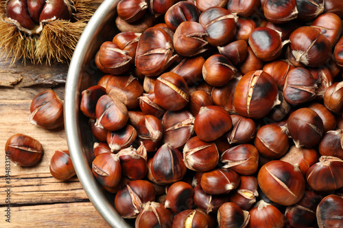 Delicious roasted edible chestnuts in bowl on wooden table, above view