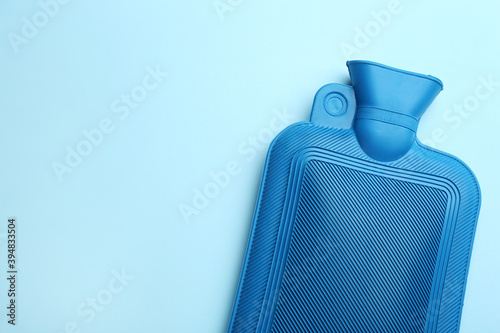Rubber hot water bottle on light blue background, top view. Space for text