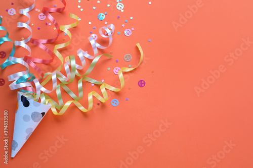 Vászonkép Colorful confetti and streamers with party cracker on orange background, top view