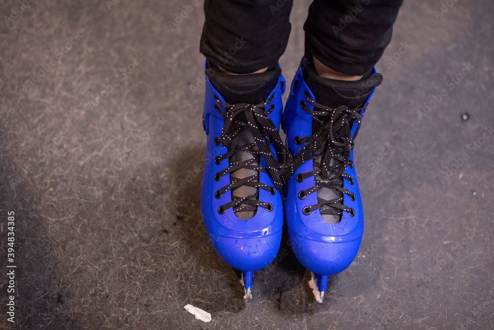 Bright blue skates on a special ice rink surface. Water droplets and ice pieces. Sports shoes for hockey or figure skating. The concept of winter sports activities. Close-up photo, copy space