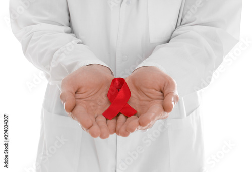 Doctor holding red awareness ribbon on white background, closeup. World AIDS disease day