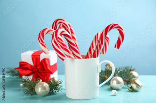 Many sweet candy canes in cup and Christmas decor on light blue wooden table