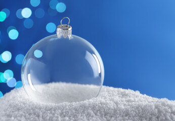Transparent Christmas ball on snow against blurred fairy lights, space for text