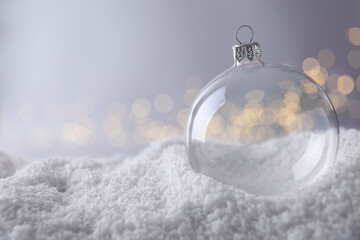 Transparent Christmas ball on snow against blurred fairy lights, space for text