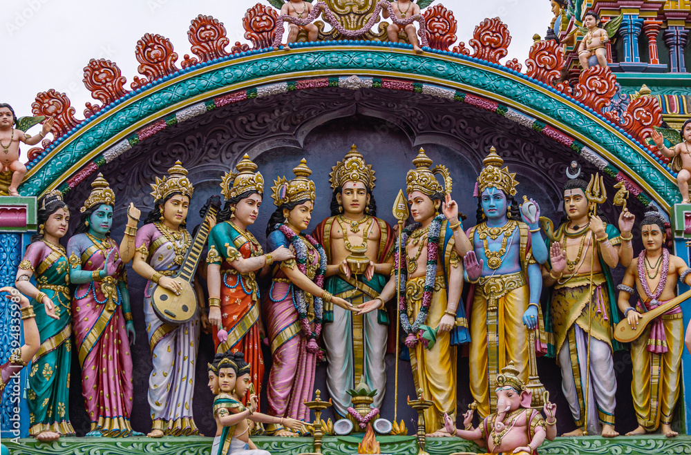 Kadirampura, Karnataka, India - November 4, 2013: Sri Murugan Temple. Closeup of colorful statues together representing wedding of Murugan set on top facade under blue cloudscape.