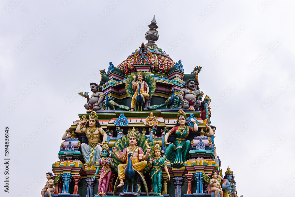 Kadirampura, Karnataka, India - November 4, 2013: Sri Murugan Temple. Colorful statues on top of gopuram against silver cloudscape. Twice Murugan on peacock. At bottome this 2 wives.