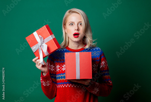 Beautiful woman in Christmas sweater with gift box on green background © Masson
